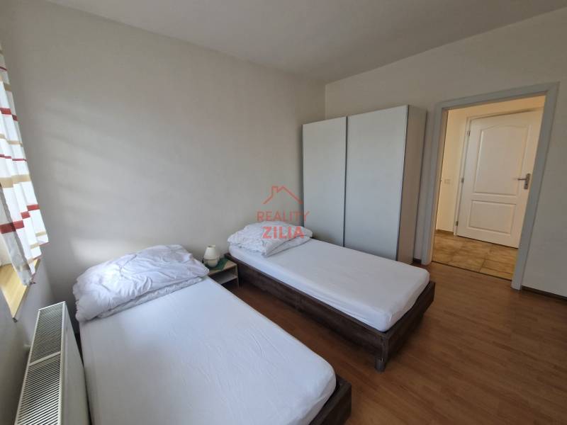 Szoba egy családi házban két ággyal, szekrénnyel és fa mintázatú padlóval.