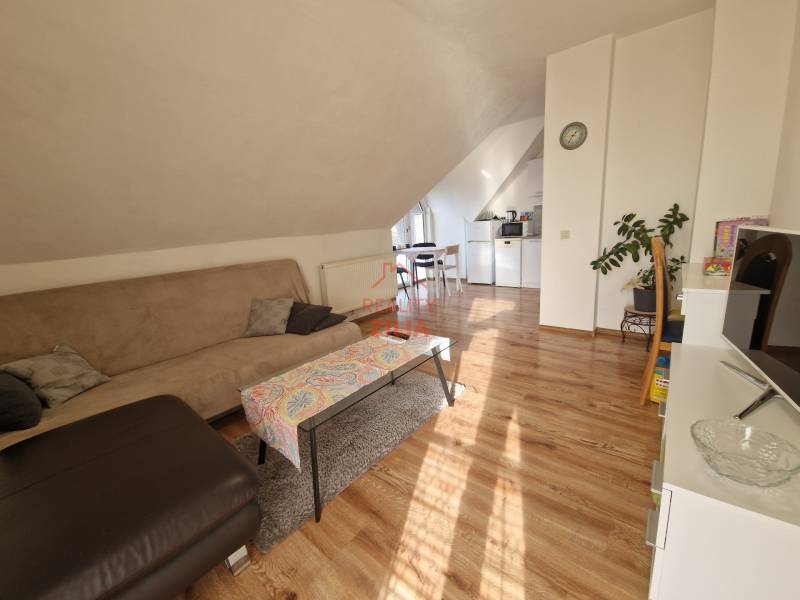 Családi ház tetőtéri nappalija kanapéval, étkezőasztallal és fa dekorációjú padlóval.