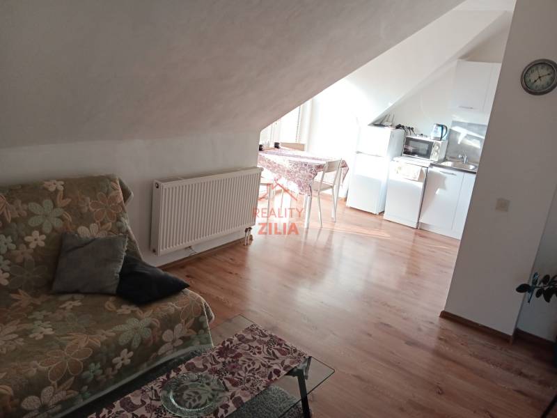 Családi ház tetőtéri helyisége konyhával, virágmintás kanapéval és fa dekorációjú padlóval.