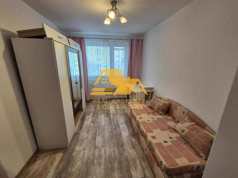 Szoba egy háromszobás lakásban kanapéval, szekrénnyel és fa dekor padlóval.