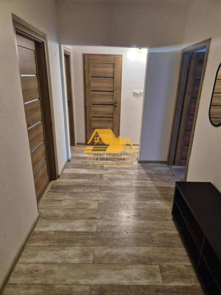 Folyosó egy háromszobás lakásban, fa dekorációjú padlóval és több ajtóval.