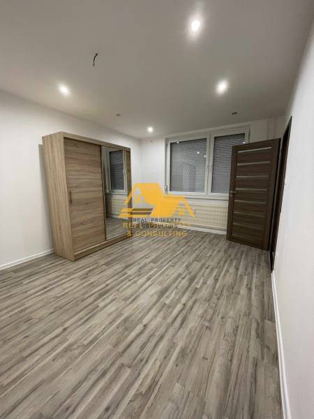 Tágas szoba tolóajtós szekrénnyel és fa dekoros padlóval egy egyszobás lakásban.