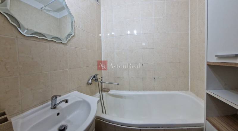 Fürdőszoba egy kétszobás lakásban káddal, mosdóval és tükörrel, bézs csempével burkolva.