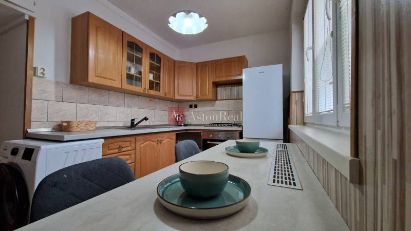 Konyha fa szekrényekkel és étkezőasztallal egy kétszobás lakásban.