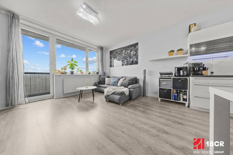 Nappali rész egy kétszobás lakásban kanapéval, asztallal és fa dekorációjú padlóval.