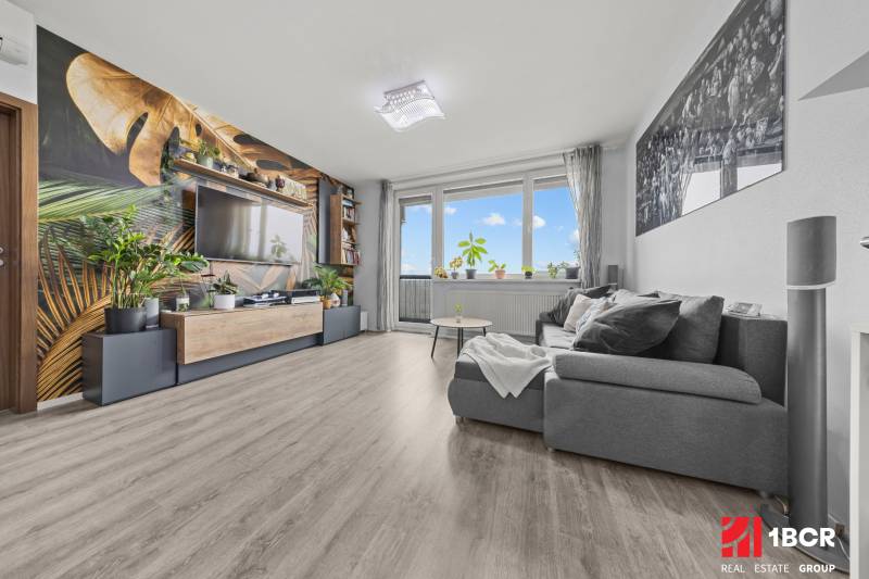 Nappali kényelmes kanapéval, növényi mintás tapétával és fa dekorációjú padlóval.