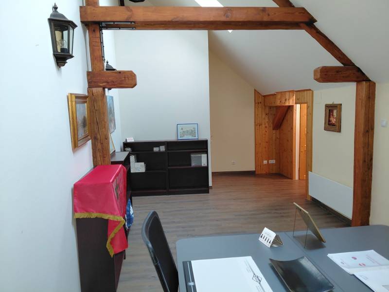 Gerendás mennyezetű és fa dekorációjú padlójú irodák, polcok takaróval, asztal dokumentumokkal.