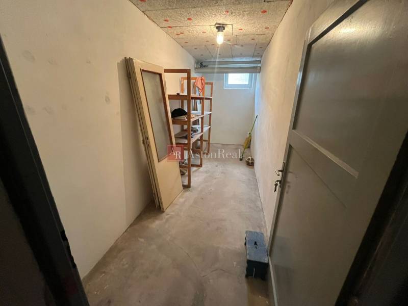 Tároló polcokkal és ablakkal egy háromszobás lakásban, padlóburkolat nélkül.