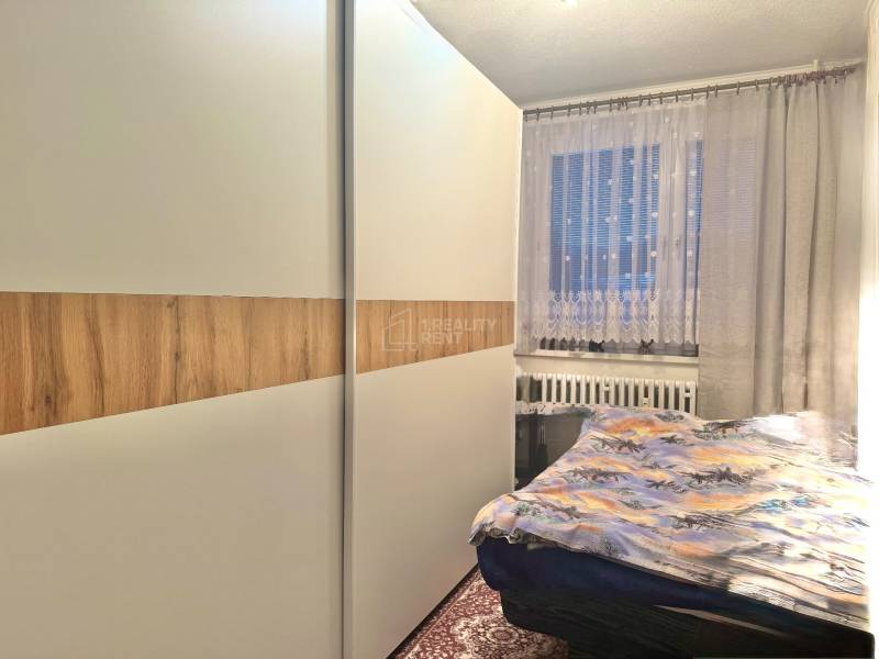 Hálószoba egy kétszobás lakásban nagy szekrénnyel és dekoratív függönyökkel ellátott ablakkal.