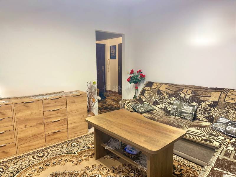 Nappali egy kétszobás lakásban fa komóddal és mintás szőnyeggel.