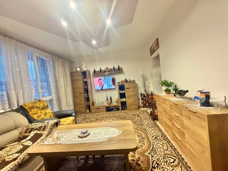 Nappali egy kétszobás lakásban, ízléses fotellel, televízióval és szőnyeggel, fa dekoros padlóval.