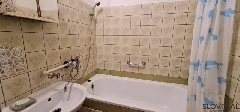 Fürdőszoba tükörrel és káddal egy háromszobás lakásban, dekoratív csempével burkolva.