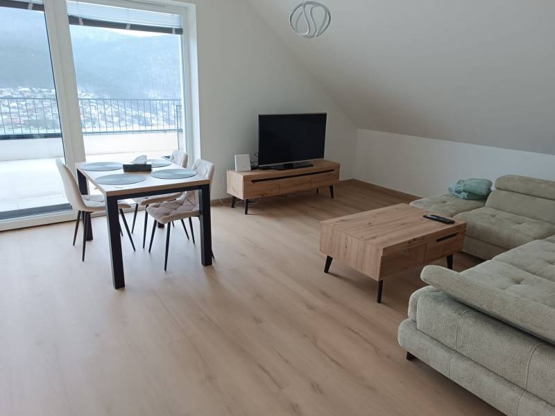 Nappali egy kétszobás lakásban, fa hatású padlóval, étkezőasztallal és kanapéval.