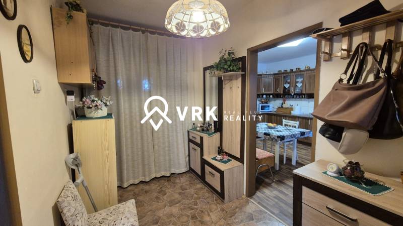 Családi ház előszobája fogassal, tükörrel és bejárattal a konyhába, ahol étkezőasztal található.