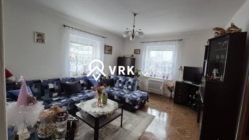 Családi ház kanapéval, szekrénnyel, televízióval, dekorációkkal és fa mintázatú padlóval.