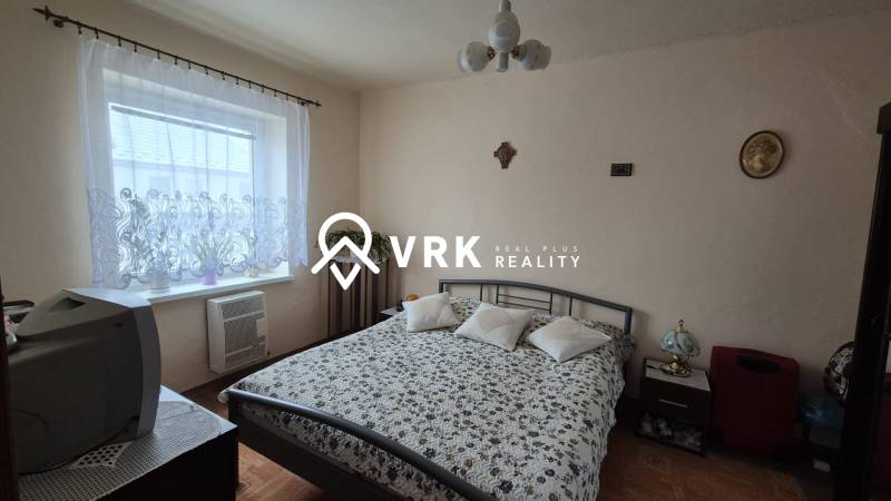 Hálószoba családi házban mintás ágytakaróval, televízióval és fa dekorációjú padlóval.