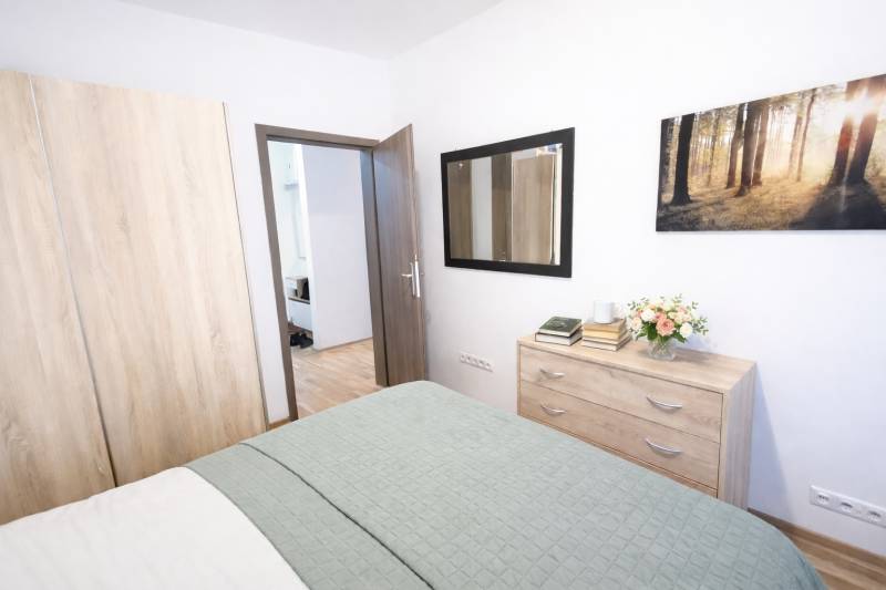 Hálószoba egy kétszobás lakásban szekrénnyel, komóddal és fa dekor padlóval.