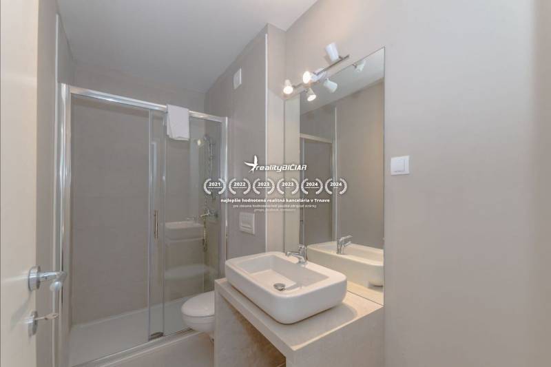 Fürdőszoba a nyaraló apartmanban mosdóval, zuhanyzóval és nagy tükörrel.