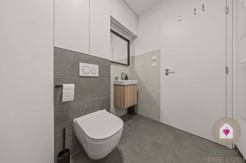 Fürdőszoba WC-vel és mosdóval egy 4 szobás lakásban, szürke csempékkel, praktikus tárolóhelyekkel.