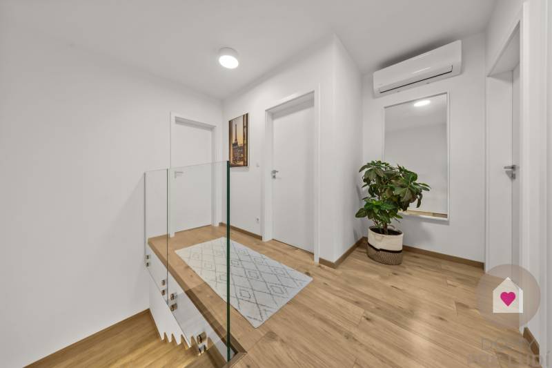 Folyosó egy 4 szobás lakásban fa mintás padlóval, tükörrel és növénnyel.