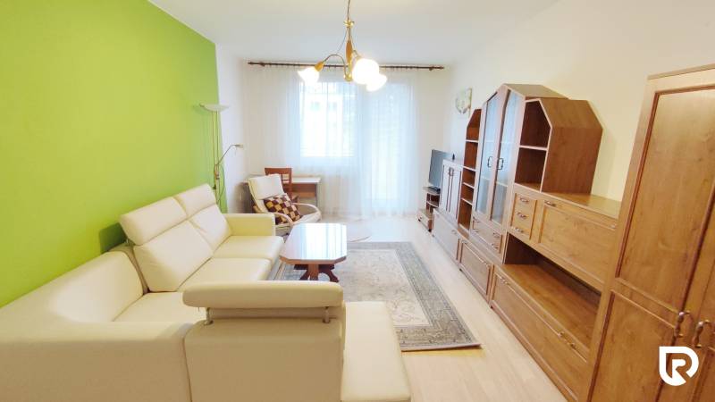 Nappali egy kétszobás lakásban krémszínű kanapéval, zöld fallal és bútorszettel.