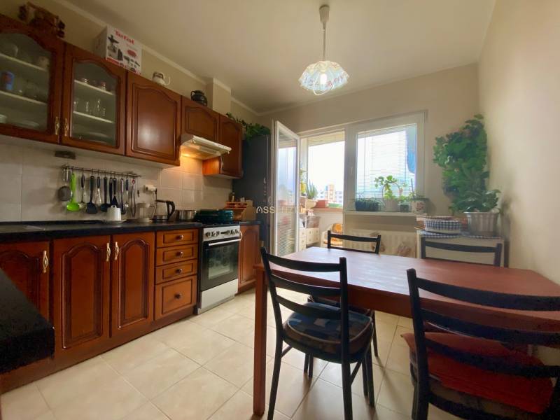 Konyha egy háromszobás lakásban fa szekrényekkel, étkezőasztallal és erkéllyel rendelkező ablakkal.