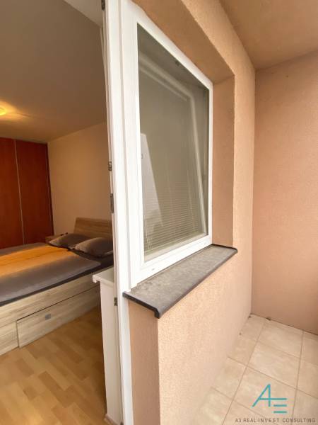 Hálószoba egy kétszobás lakásban ággyal, fa dekorációjú padlóval és teraszra nyíló hozzáféréssel.