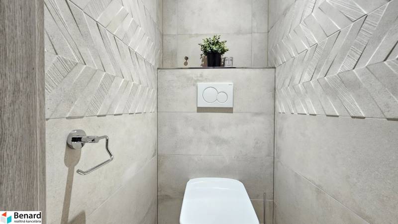 Fürdőszoba egy egyszobás lakásban modern burkolatokkal és dekoratív növénnyel.