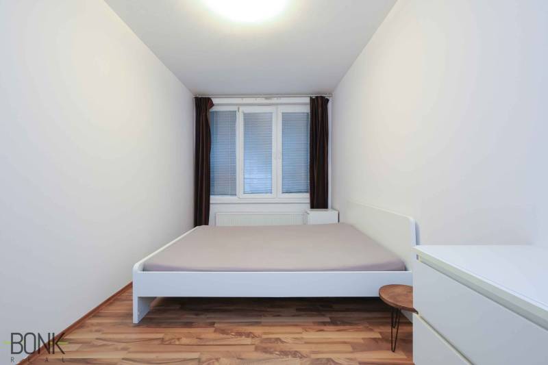 Hálószoba egy kétszobás lakásban fehér bútorokkal és fa dekorációjú padlóval.