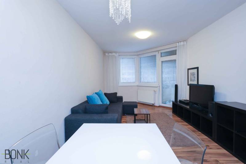 Nappali egy kétszobás lakásban kanapéval, televízióval és fa dekorációjú padlóval.