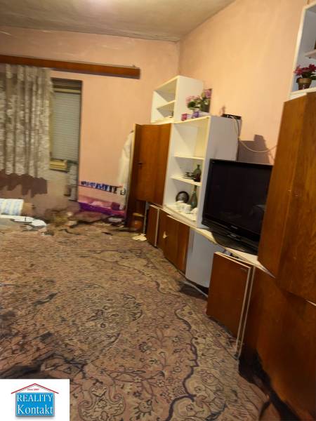 Szoba családi házban szőnyeggel, polcokkal, televízióval és függönyökkel.