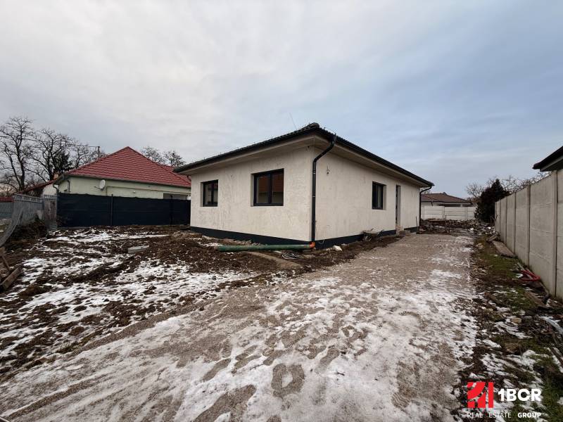 Családi ház Szencen, gondozatlan havas telekkel és beton járdával.