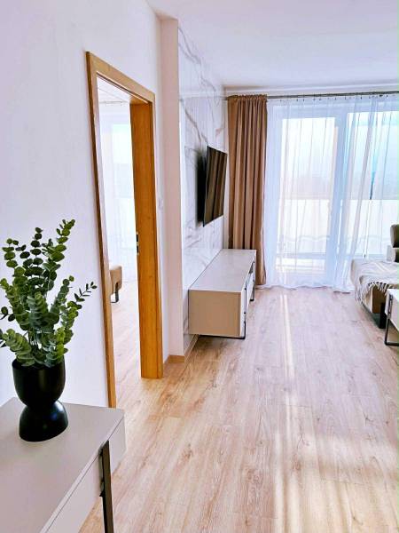 3 szobás lakás belső tere fa dekor padlóval, TV-vel és függönyökkel.