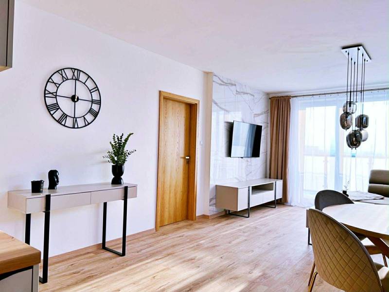 Nappali egy háromszobás lakásban, fa dekoros padlóval, asztallal és televízióval.