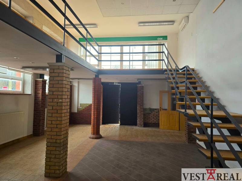 Kereskedelmi helyiségek fa mintázatú padlóval és téglából készült oszlopok melletti lépcsővel.