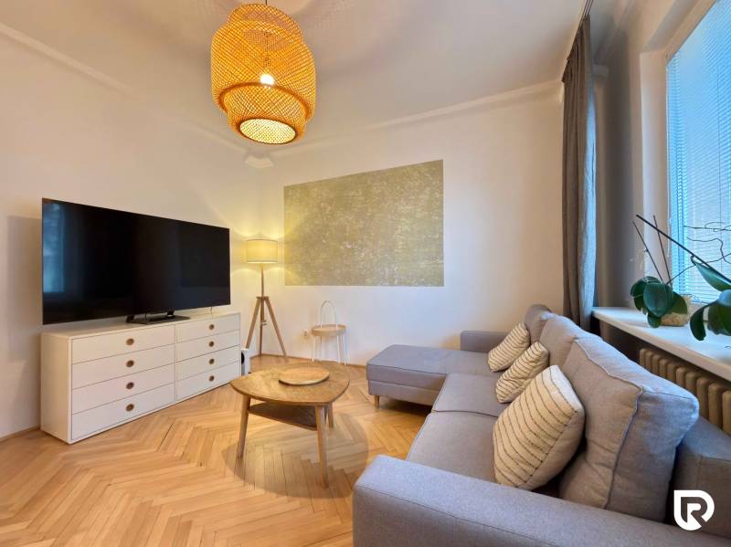 Nappali egy kétszobás lakásban fa mintázatú padlóval, kanapéval és TV-vel.