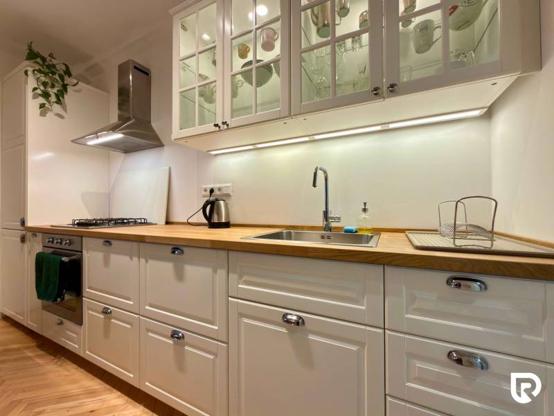 Világos konyha egy kétszobás lakásban, fa mintázatú padlóval és fehér szekrényekkel.