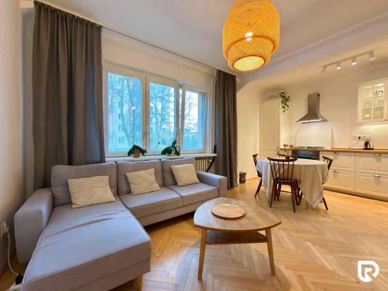 Nappali konyhával és étkezőasztallal, fa dekorációjú padló, világos kanapé.