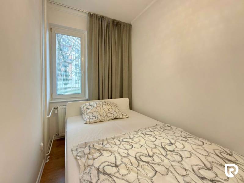 Hálószoba egy kétszobás lakásban ággyal, ablakkal és függönyökkel, fa dekorú padlóval.