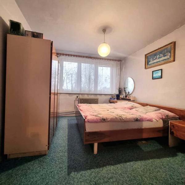 Hálószoba egy háromszobás lakásban, franciaággyal, szőnyeggel, bútorokkal és függönyökkel az ablakon.