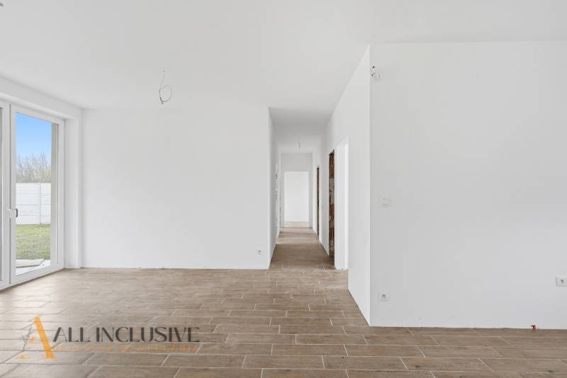 Fehér folyosó egy családi házban, fa dekorációjú padlóval és üvegezett ajtókkal az udvarra.