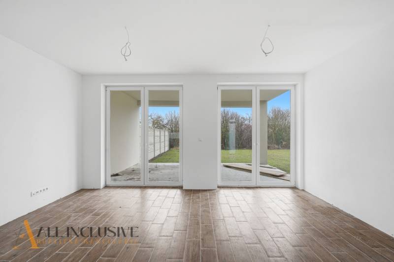 Egy családi házban van egy tágas szoba nagy ablakokkal és fa dekorációjú padlóval.