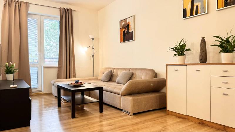 Nappali egy kétszobás lakásban bézs kanapéval, fa mintázatú padlóval.