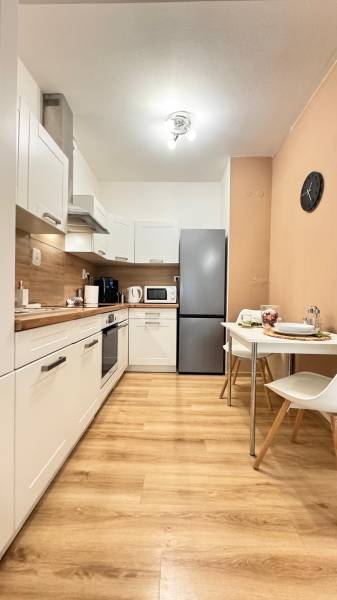 Konyha egy kétszobás lakásban fehér szekrényekkel és fa hatású padlóval.