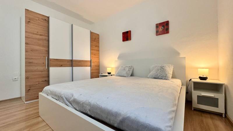 Hálószoba egy kétszobás lakásban nagy ággyal, gardróbszekrénnyel és fa dekoros padlóval.