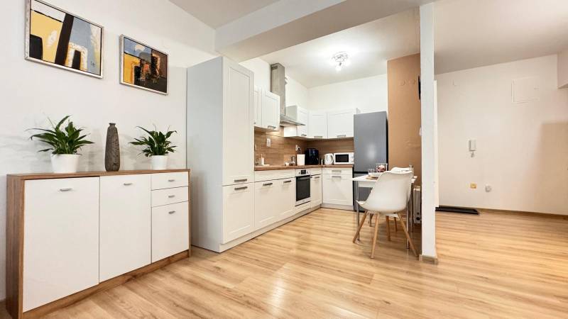 Konyha egy kétszobás lakásban fehér szekrényekkel és fa mintázatú padlóval.