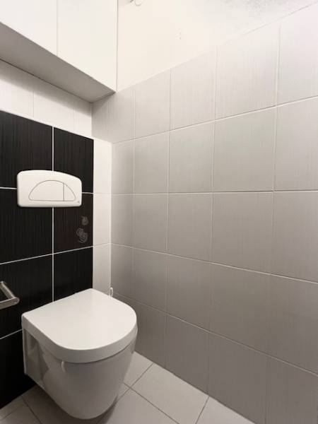 WC egy kétszobás lakásban, fehér és fekete csempékkel a falakon.