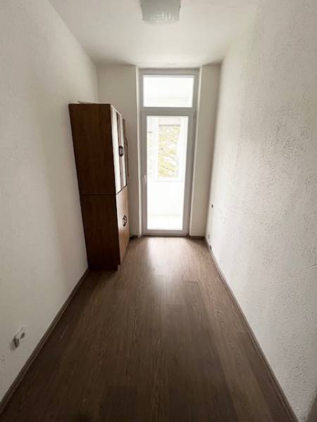 Keskeny belső tér egy kétszobás lakásban, fa dekoros padlóval és szekrénnyel.