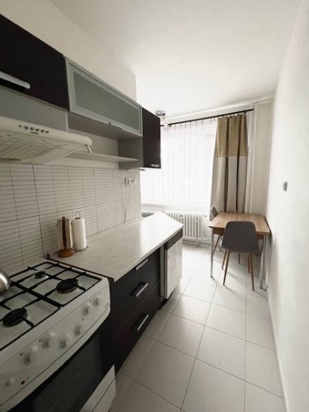 Konyha egy kétszobás lakásban tűzhellyel, sötét bútorokkal és világos csempével.