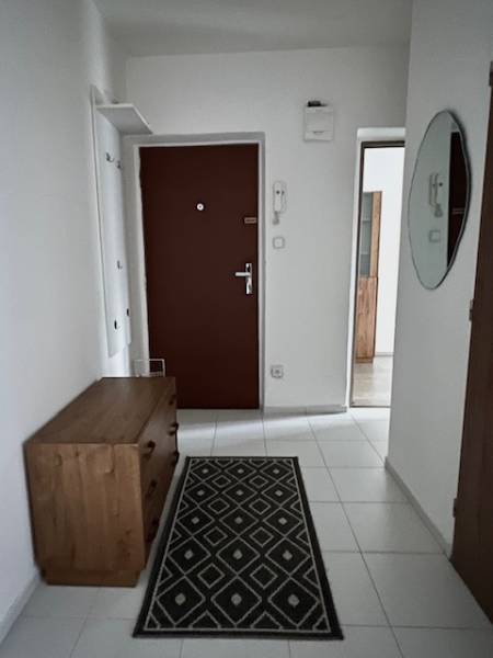 Folyosó egy kétszobás lakásban fehér csempével és fa berendezéssel.